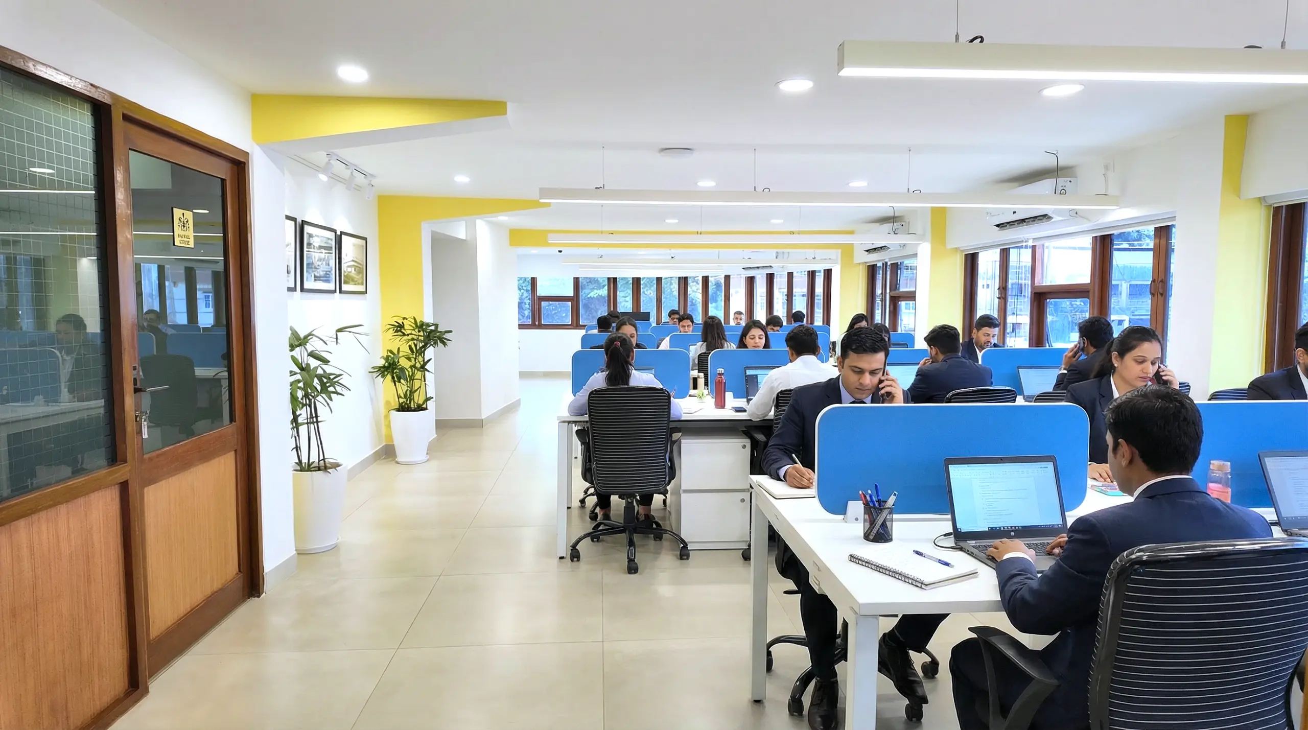 Open Area in a coworking space at Kowo Workspaces with shared desks, blue privacy panels, and professionals working in a bright, collaborative office environment.
